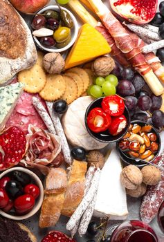 Festive gourmet mix of snacks and appetizers, cheese, meat, olives, bread, fruit, canapés, wine in glasses. Italian antipasti set or Spanish tapas bar. Food to share, party or picnic time, top view.