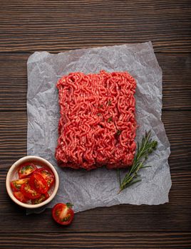 Fresh raw minced meat from ground beef or pork with ingredients for cooking on cutting board and dark brown rustic wooden background from above