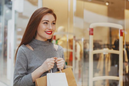 Beautiful happy young woman enjoying shopping at the mall, carrying bags with purchase, looking away joyfully, copy space