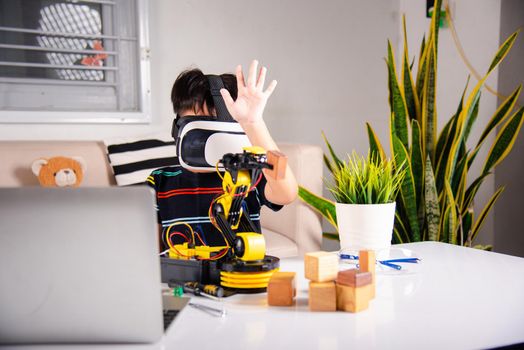 Asian kid boy using VR glasses on robotic arm in workshop, Child learning programer control robot arm with sensors to pick up wood block, Technology education, Virtual Reality Simulator, industry 4.0