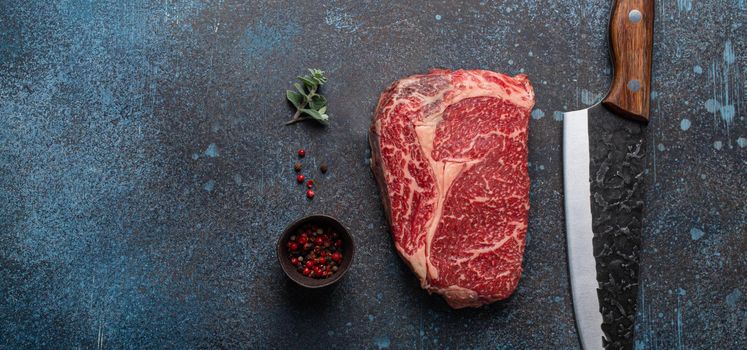 Raw meat beef marbled prime cut steak Ribeye on rustic concrete kitchen table background from above with big knife and spices, beefsteak concept space for text