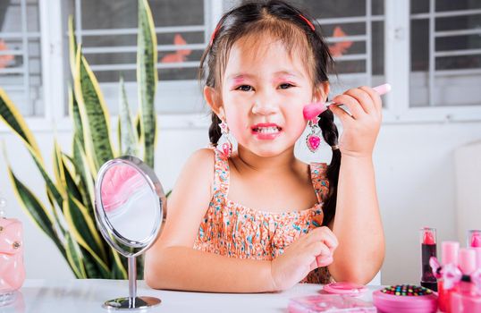 Happy kid is beautiful make up with cosmetics toy, Asian adorable funny little girl making makeup her face she looking in the mirror and cheek fluffy brush for powder, Learning activity to be woman