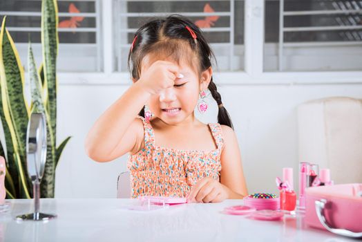 Happy kid is beautiful make up with cosmetics toy, Asian adorable funny little girl making makeup her face she applying carborundum eyeliner to eyelid, Learning activity to be woman at house