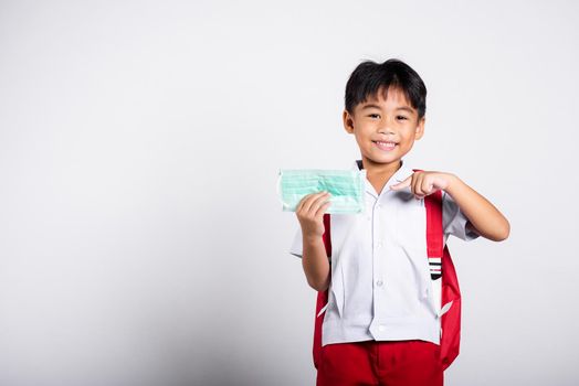 Asian student kid boy wearing student thai uniform and pointing finger to protect mask before to go to school in studio shot isolated on white background, preschool, new normal back to school