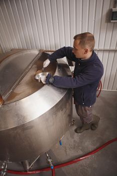 Vertical top view shot of a brewery worker checking fermenting beer in a barrel