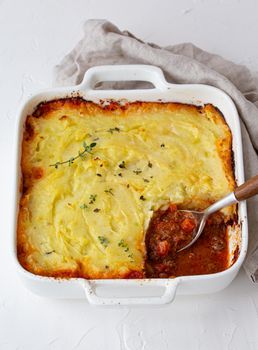 Traditional dish of British cuisine Shepherd's pie casserole with minced meat and mashed potatoes in ceramic baking dish on white rustic table with spoon from above