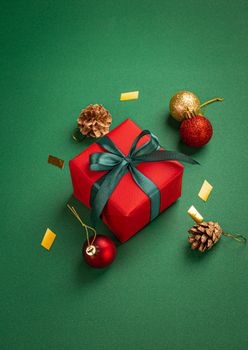 Christmas present box wrapped in red paper with green ribbon and bow, Christmas sparkly round balls decorations on green paper background angle view, Christmas composition in red, green and golden