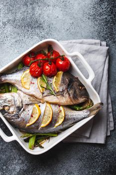 Baked fish dorado with green asparagus and tomatoes in white ceramic baking pan on gray rustic concrete background, top view. Healthy dinner with fish concept, dieting and clean eating .