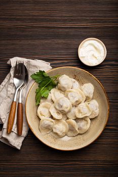 Pelmeni, traditional dish of Russian cuisine, boiled dumplings with minced meat filling on plate with sour cream sauce on wooden rustic background table from above food composition