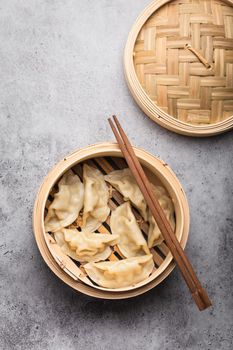 Close-up, top view of traditional Asian dumplings in bamboo steamer with chopsticks on gray rustic stone background. Authentic Chinese cuisine