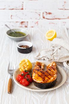 Grilled salmon steak glazed with teriyaki sauce, vegetables and lemon served on ceramic plate on rustic white wooden table from angle view, selective focus