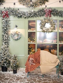 Christmas studio decorations outside in green tones with a bench and plush toy near cafe bakery, door, wreaths, lanterns, garland, glass showcase with ginger bread, windows and many fir trees in snow