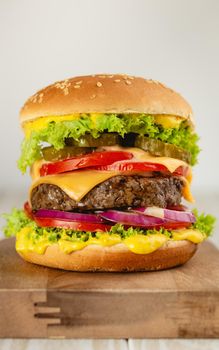 Delicious burger with meat, melted cheese, dripping sauce and vegetables on white rustic background. Freshly made tasty hamburger, close-up.