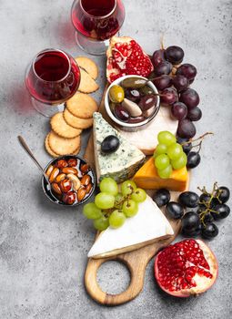 Selection of cheese and appetizers, wine in glasses, camembert, brie, cheddar, cracker, grapes, nuts, honey. Assorted mix of cheese on rustic wooden board, top view, close-up.