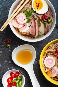 Cooking Japanese noodle soup ramen. Ramen with sliced pork, narutomaki, egg and kitchen spoon with broth on rustic stone background. Making traditional dish of Japan, top view, close-up, concept