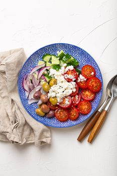 Greek mediterranean salad with tomatoes, feta cheese, cucumber, whole olives and red onion in ceramic plate on white stone background from above, traditional appetizer of Greece