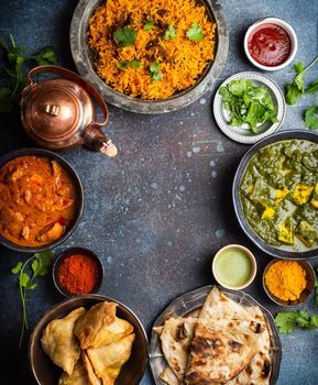 Overhead of Indian traditional dishes and appetizers: chicken curry, pilaf, naan bread, samosas, paneer, chutney on rustic background. Table with choice of food of Indian cuisine, space for text