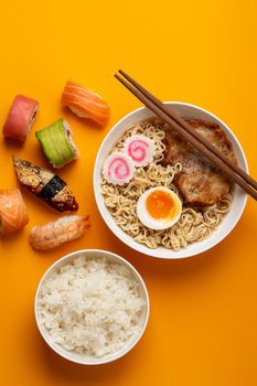 Set of traditional Japanese food: hot soup ramen, boiled white rice, sushi, fish rolls on bright orange background. Dishes of Japanese cuisine, from above, asian style dinner or lunch.