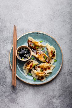 Close-up, top view of traditional Asian dumplings in blue plate with soy sauce and chopsticks on gray rustic stone background. Authentic Chinese cuisine