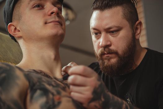 Cropped shot of a bearded mature male tattoo artist concentrating while freehand sketching tattoo on the chest of a client. Young man getting new chest tattoo. Concentrated tattooist working