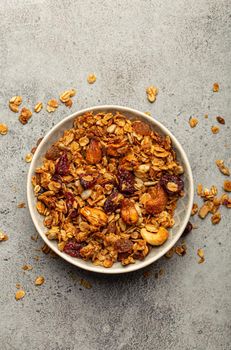 Bowl with crispy homemade granola, healthy breakfast cereal granola with oatmeal, seeds, nuts, berries on rustic stone background from above.