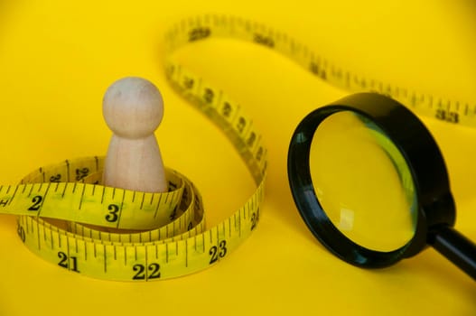 Wooden doll wrapped with yellow measuring tape with customizable space for text or ideas. Copy space and weight loss concept.