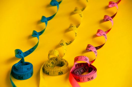 Blue, yellow and red measuring tape on yellow background. Copy space and weight loss concept.