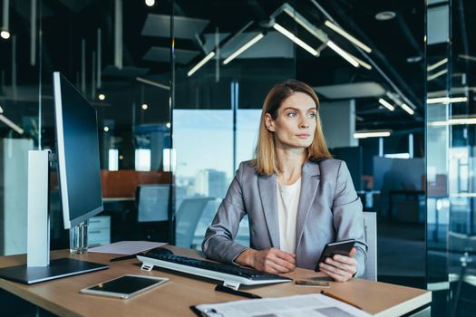 Successful woman working in a modern office on a computer, businesswoman uses the phone, social networks, online browsing