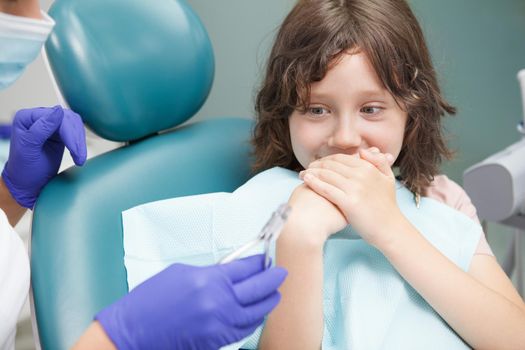 Close up of a scared boy covering his mouth with his hands, afraid of dental treatment