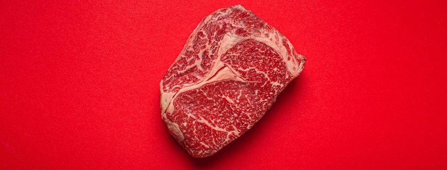 Raw fresh uncooked meat beef prime cut steak Ribeye on clean red background from above, beefsteak concept banner minimalism