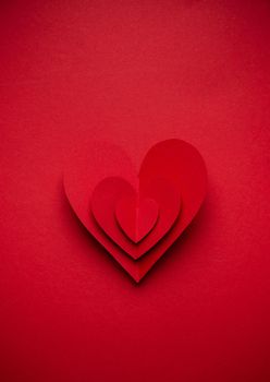 Big voluminous red heart cut from paper on red monochrome background, paper craft origami style, from above. Romantic Valentine's day symbol, love concept. Paper art design, 14 February celebration.