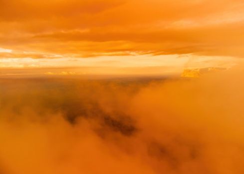 A red burning sunset with the silhouette of a cliff over the sea. Abstract nature summer or spring ocean sea background. Small waves on golden warm water surface with bokeh lights from sun.