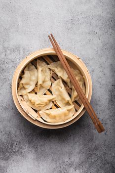 Close-up, top view of traditional Asian dumplings in bamboo steamer with chopsticks on gray rustic stone background. Authentic Chinese cuisine