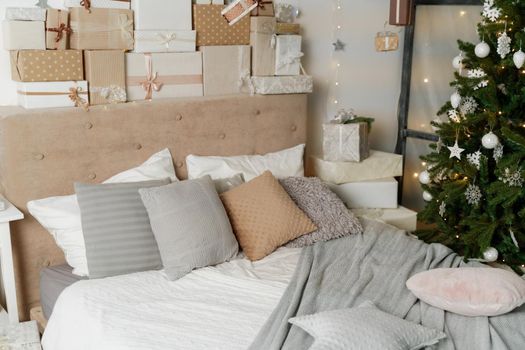 Pile of Christmas gifts in colorful wrapping with ribbons against a white wall with silver stars. Christmas tree in the room