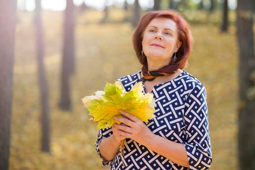 Fifty year old woman with a bouquet of autumn leaves in the park.Autumn age