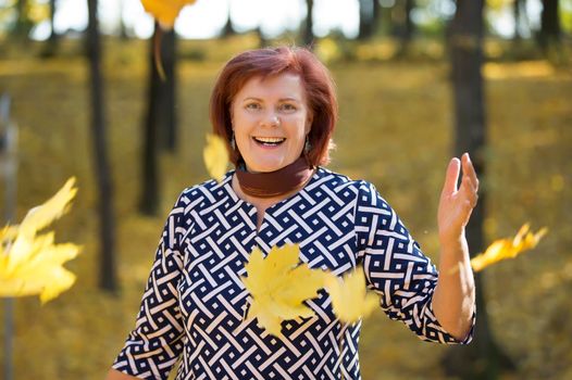 Cheerful elderly woman with autumn leaves in the park.Autumn age