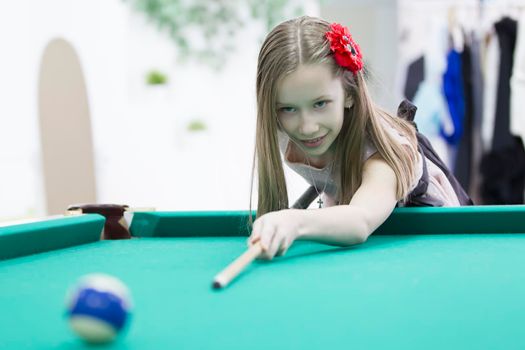 A teenage girl is playing billiards. Interesting game. A useful lesson for a child