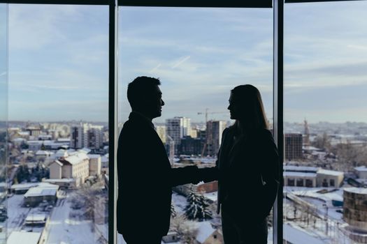 Silhouettes of two employees team of businessmen, Asian man and woman are consulting and communicating, working in a modern office by the window