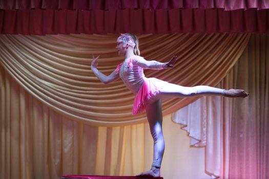 Beautiful girl acrobat gymnast performs on stage.