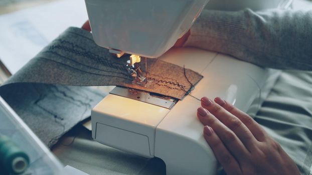 Close-up view of modern electric sewing machine working stitching piece of fabric. Young girl's manicured hand and colorful sewing threads are visible.