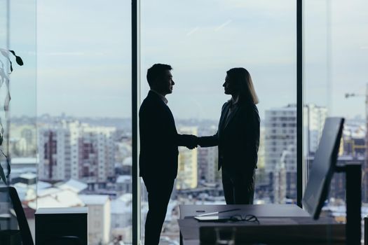 Silhouettes of two employees team of businessmen, Asian man and woman are consulting and communicating, working in a modern office by the window