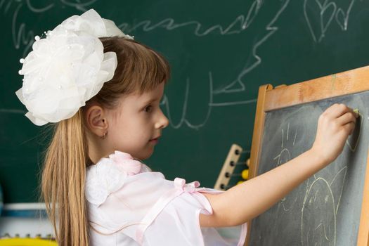 Schoolgirl of primary classes. Draw at the blackboard. Education at school. Girl with bows