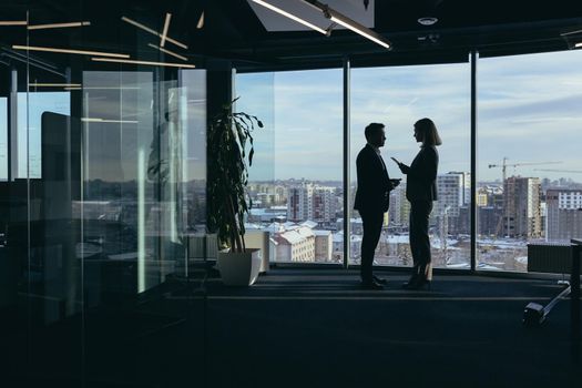 Silhouettes of two employees team of businessmen, Asian man and woman are consulting and communicating, working in a modern office by the window