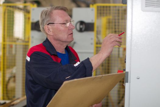 An elderly male plant worker writes a plan with a pencil. Worker at the factory