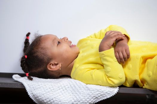 A little African American girl in a yellow dress lies on the floor and smiles.