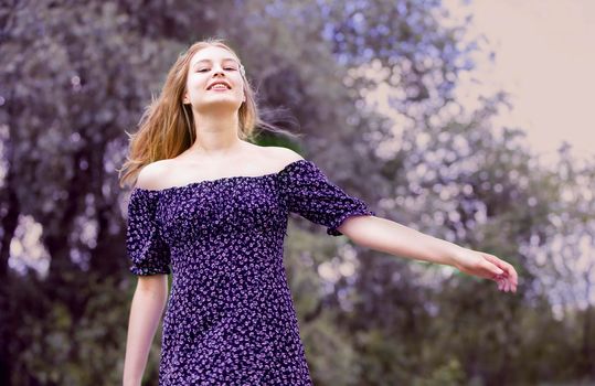 Happy young girl in a romantic dress on a green summer meadow. Beautiful teen girl smiles and looks into the camera.