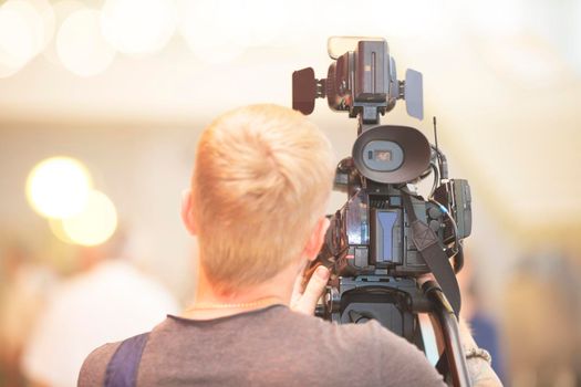 A videographer with a camera stands with his back.