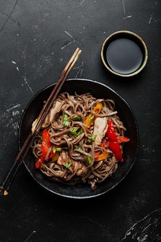 Bowl with Asian chicken stir fry soba noodles with vegetables on dark black stone background from above, Chinese Thai or Japanese noodles dish with soy sauce