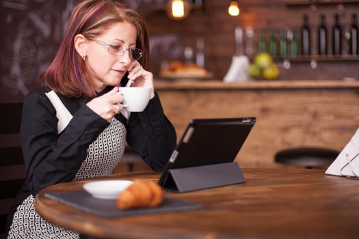 Businesswoman looking at tablet while talking having a conversation on her phone. Working in vintage coffee shop