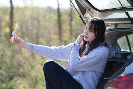 Portrait of a beautiful girl outdoors who uses a smartphone, shares digital content with each other and enjoys taking a selfie picture.